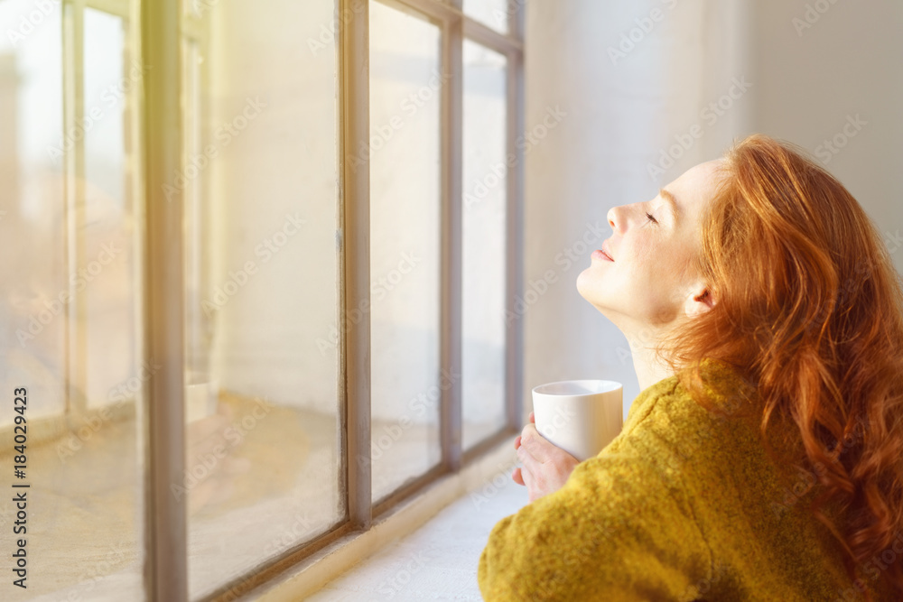 A woman looking happily and relevead from pain into the sun shining through the window in front of her