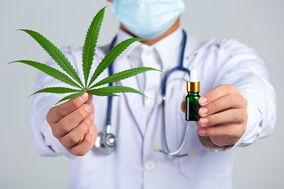 A medical doctor showing his way of therapy into the camera: a leaf of medical marijuana in the right hand an a CBD-oil in the left hand