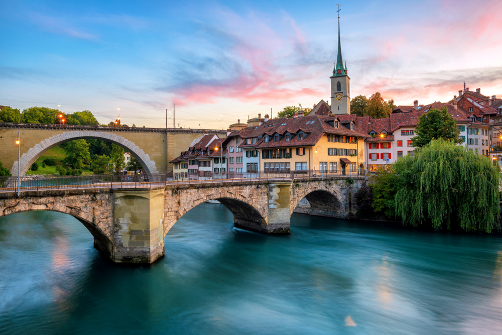 Historische Altstadt von Bern, Ziegeldächer, Brücken über die Aare und Kirchturm bei dramatischem Sonnenuntergang, Schweiz